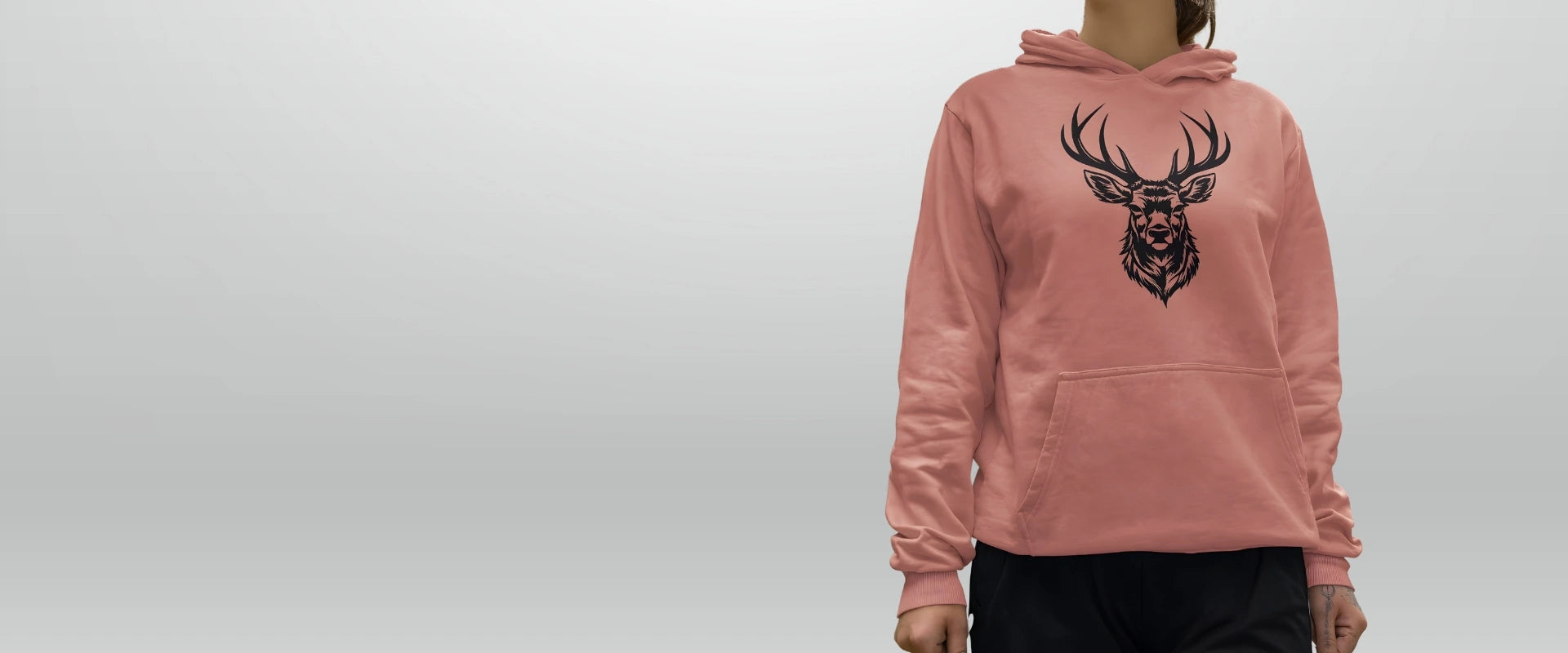 Rosa hoodie med stiliserat hjorthuvud Kvinna i rosa hoodie med stiliserat hjorthuvud – Norrländsk streetwear från Heart of North, inspirerad av vildmark och styrka från Norrland.