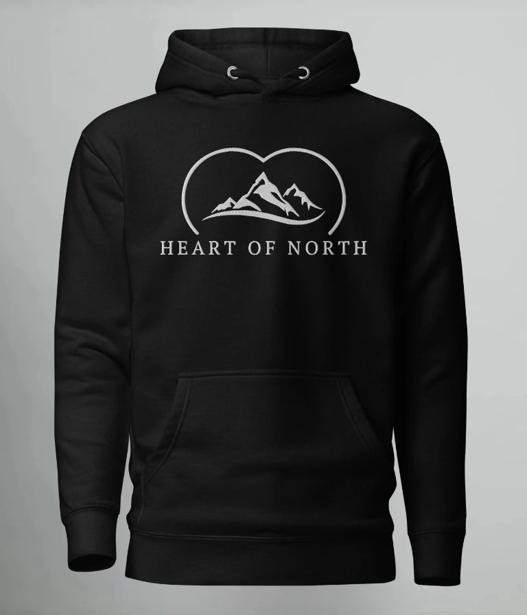 Svart hoodie från Heart of North med vit broderad logotyp föreställande fjäll och texten “Heart of North” – en exklusiv unisex-hoodie i Norrländsk streetwear-stil.