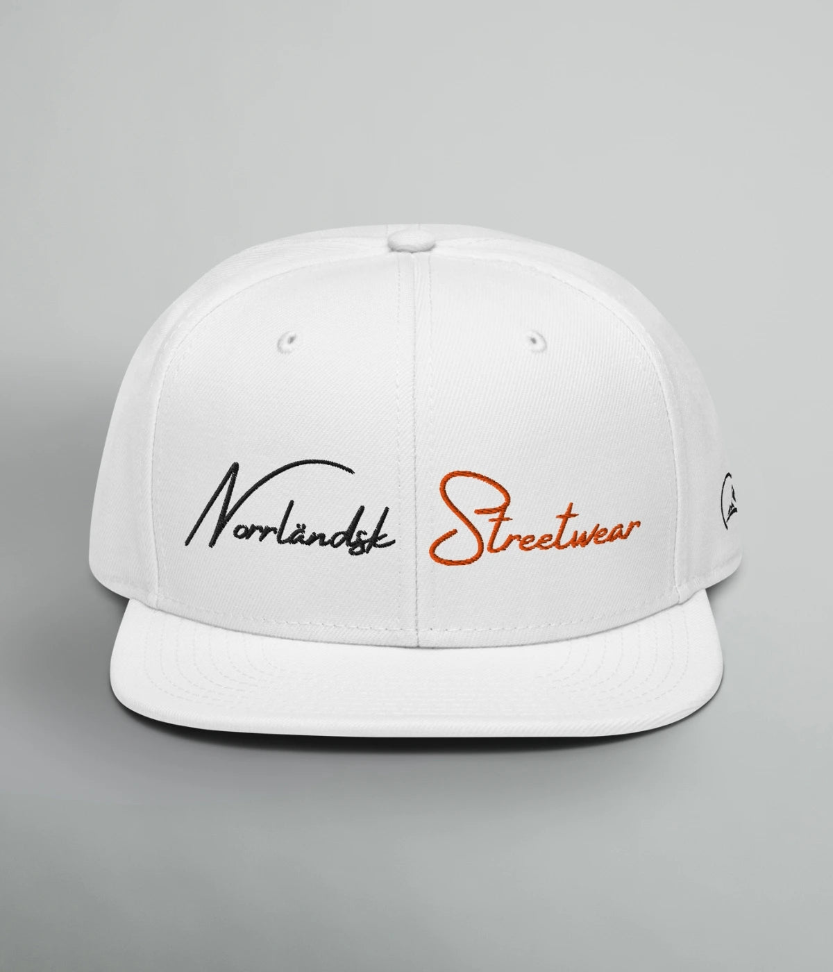 Vit Snapback-keps med texten Norrländsk Streetwear broderad i svart och orange, samt logotyp från Heart of North – unisex design inspirerad av Norrland.
