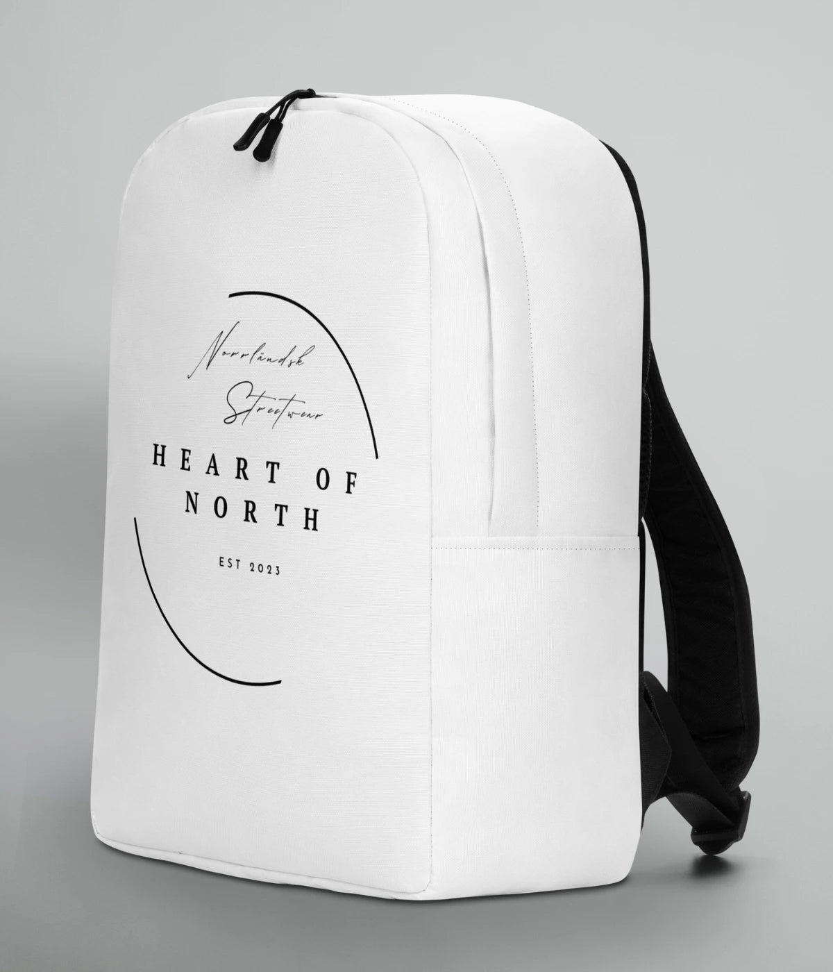 Vit ryggsäck med svart tryck från Heart of North – texten ´Norrländsk Streetwear EST 2023´ i modern design. En del av kollektionen Norrländsk streetwear.