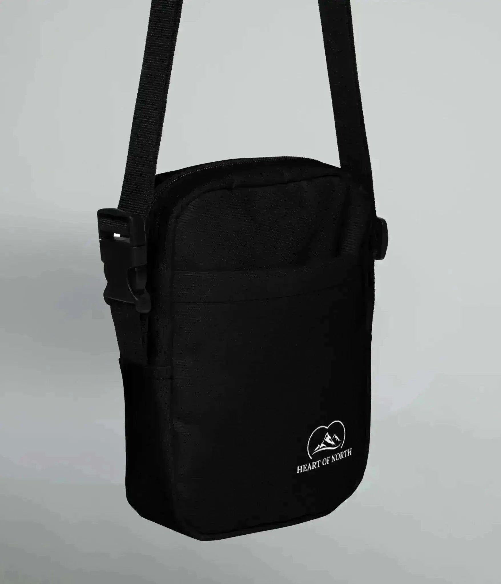 Svart Crossbody-väska från Heart of North med vit logotyp framtill, justerbar rem och kompakt design – perfekt för äventyr och vardag.